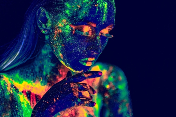 Lucida, a face and hand glowing with fluorescent pigment under ultraviolet light